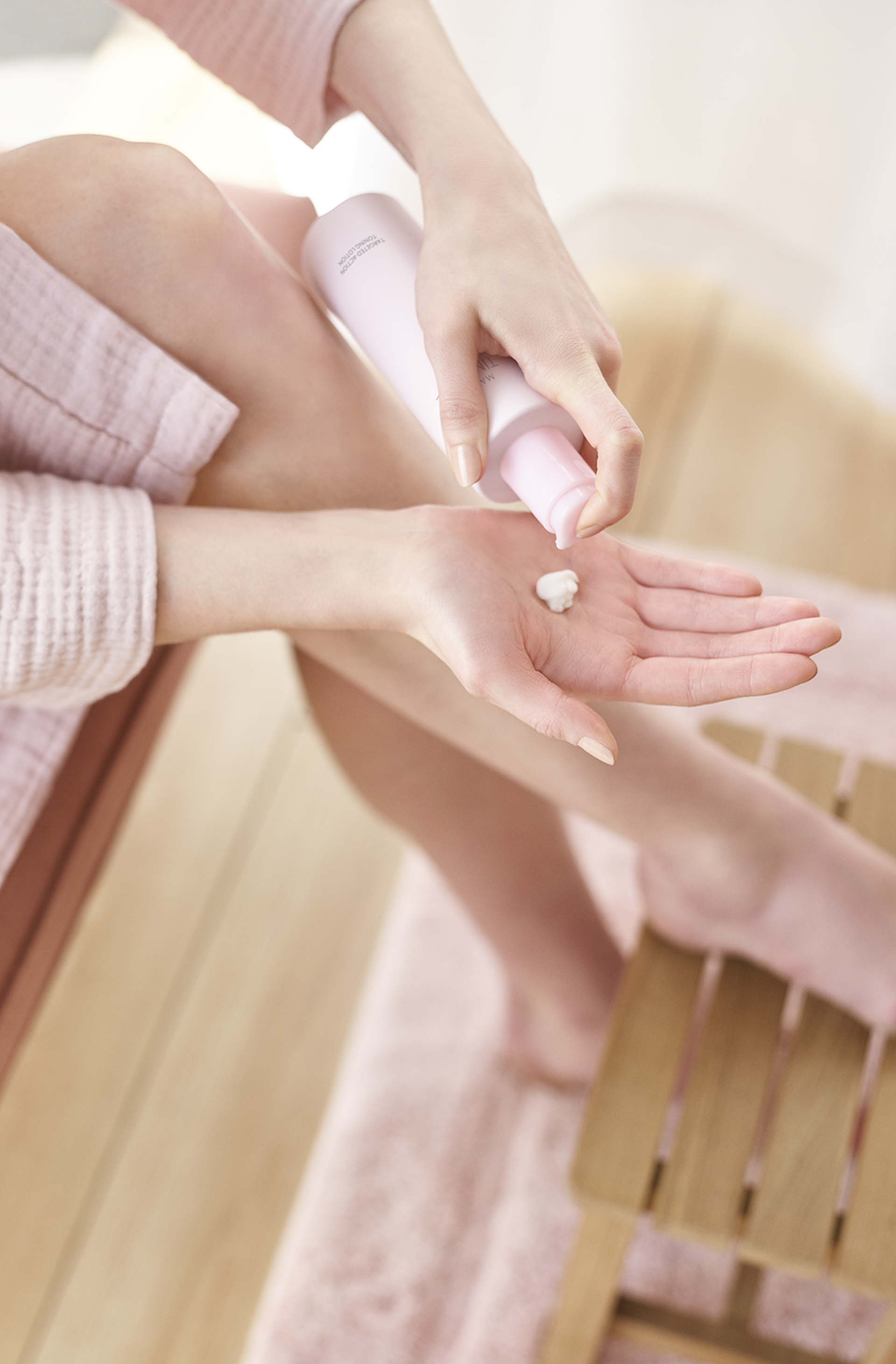 Une personne assise sur un banc en bois verse une goutte de la Lotion tonique Mary Kay dans sa paume de main.