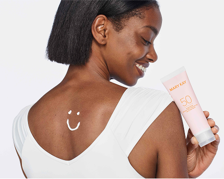 Model holding a tube of Mary Kay Sunscreen Broad Spectrum SPF 50, with a smiley face drawn using sunscreen on the upper back.