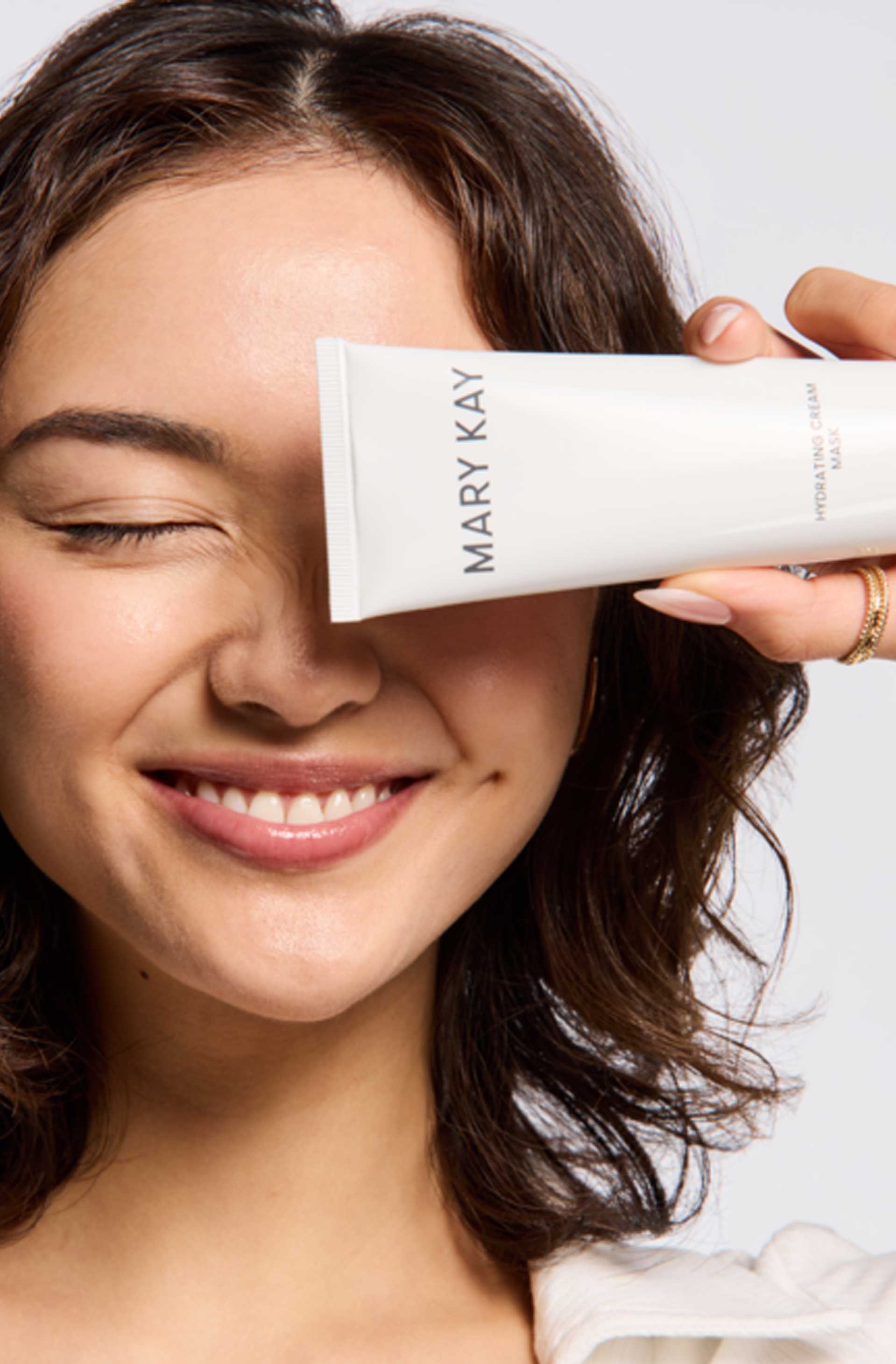Une personne tient un tube de Nettoyant Mary Kay au-dessus de son œil tout en souriant.